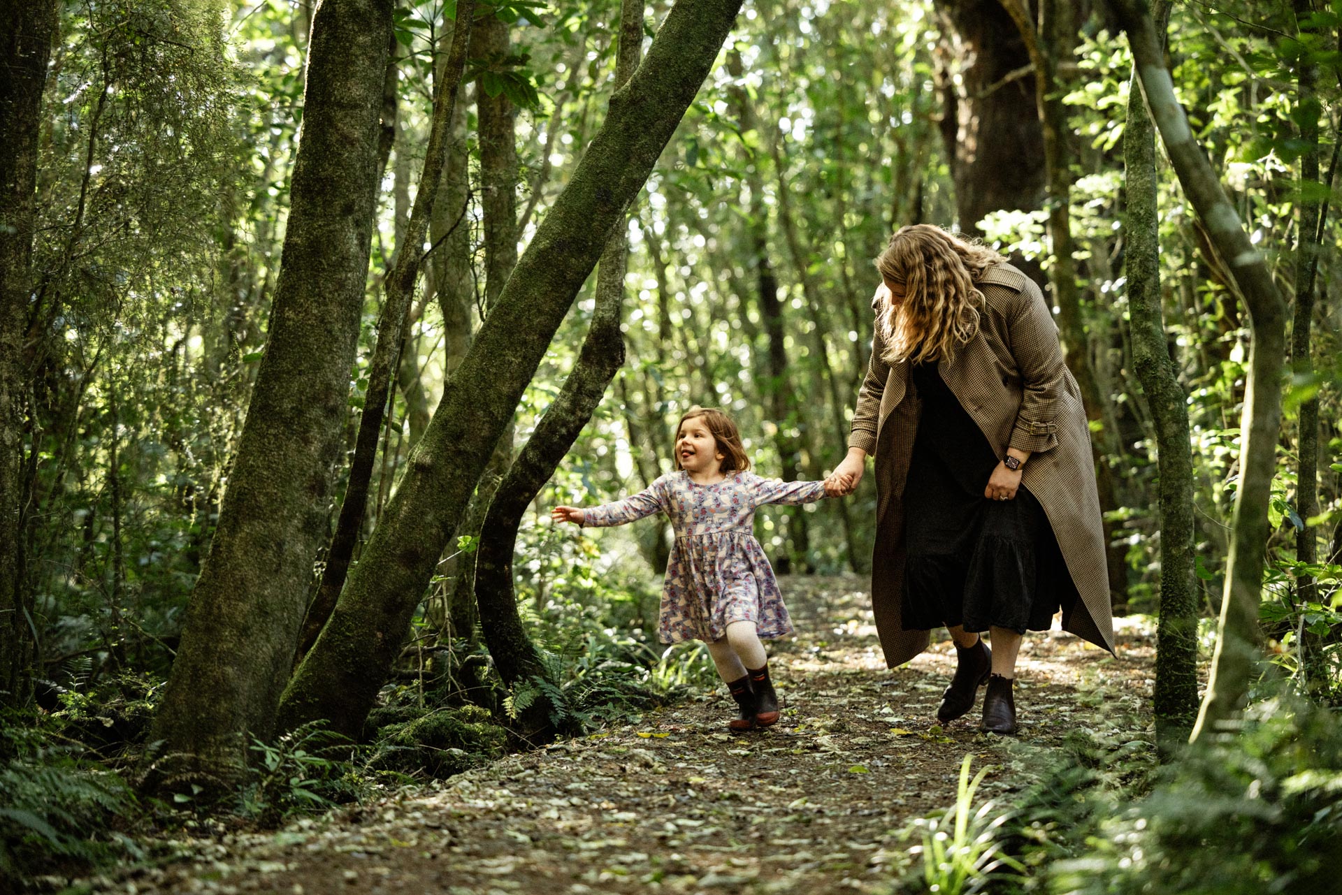 Mother and daughter walking hand-in-hand through native forest at Whakahā